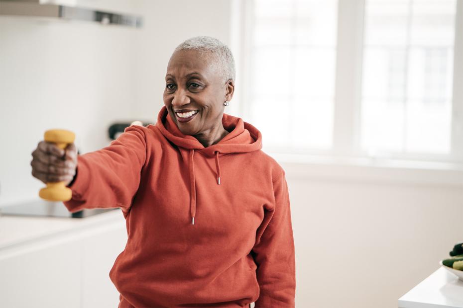 A black woman in an orange hoodie exercises with weights.